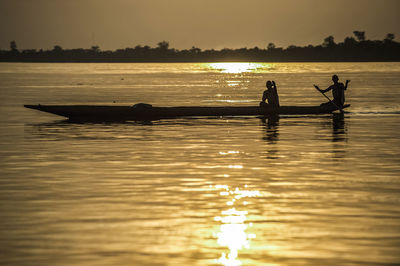 Silhouette men in boat on sea during sunset