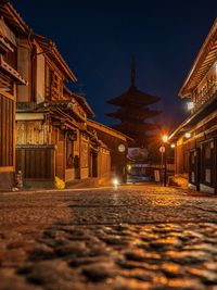 Illuminated street amidst buildings against sky at night