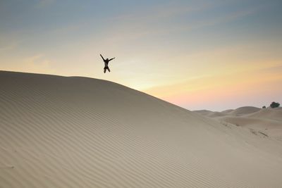 Girl jumping at desert against sky during sunset