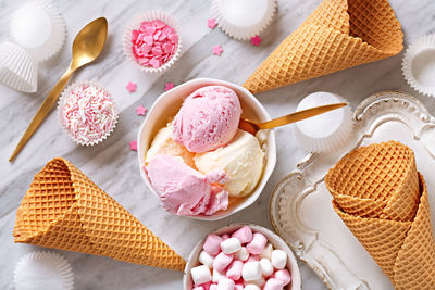 High angle view of ice cream served in bowl by candies and cones on floor