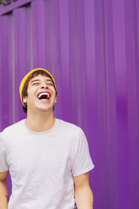 Cheerful non-binary person laughing in front of purple wall