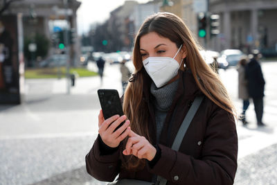 Young woman wearing mask while using mobile outdoors