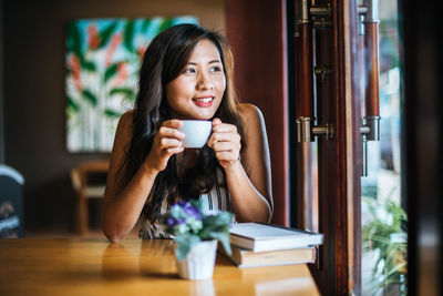 Young woman holding coffee while sitting on table