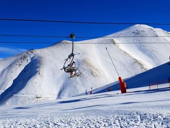 Ski lift by snowcapped mountains against blue sky