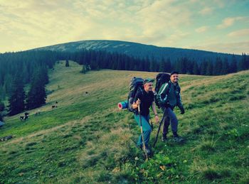 Male hikers hiking on grassy hill against sky