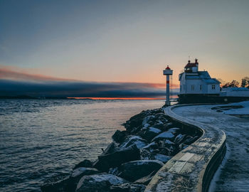 Lighthouse by sea against sky during sunset