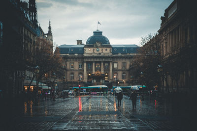 People on wet street amidst buildings in city