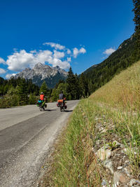 People riding road by mountains against blue sky