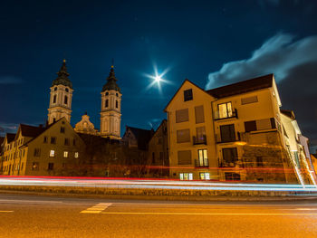 Light trails on street by buildings against sky at night