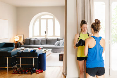 Serious athletic female in boxing gloves standing at home with personal instructor and preparing for workout