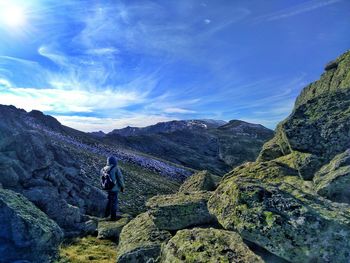 Rear view of hiker on rocks with mosses looking  at horizon over mountains