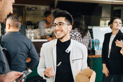 Male customer with box talking to friend while standing against food truck