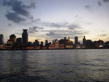 Sea by cityscape against sky during sunset