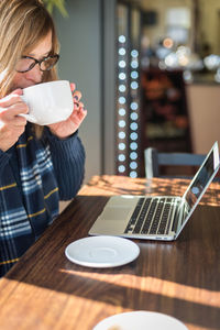 Midsection of woman holding coffee while sitting on table at cafe