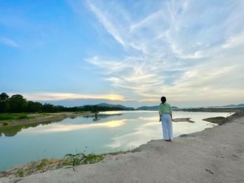 Rear view of woman standing on beach against sky