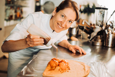 Chef is adding syrup to a dessert, looking at camera and smiling