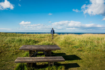 Picnic table with man walking on field in background against blue sky