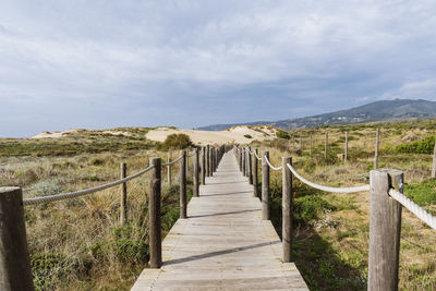 Empty, wooden boardwalk on a beach praia do guincho in sintra. view of grass and sand with hills