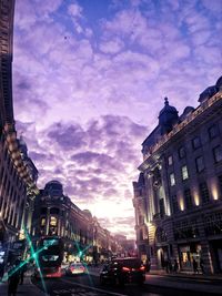 Cars on city street by buildings against sky