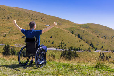 Rear view of man sitting on landscape against sky