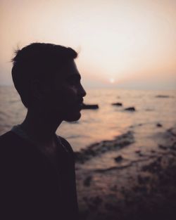 Portrait of young man on beach against sky during sunset