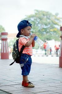 Side view of boy drinking water from plastic bottle on footpath