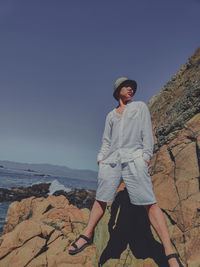 Portrait of young man standing on rock against clear sky