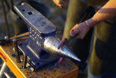 Midsection of blacksmith holding horseshoe on anvil