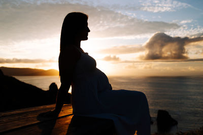 Silhouette woman sitting against sea and sky during sunset