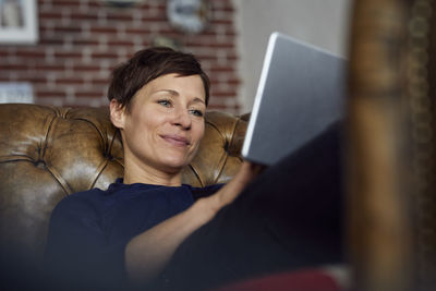 Woamn sitting on sofa at home, using digital tablet