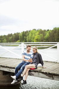 Couple using mobile phone together on pier