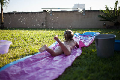 Girl lying on grassy field against sky