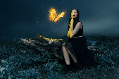 Young woman looking away while sitting on land