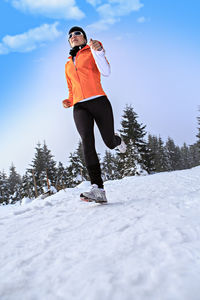 Woman running on snow covered field against sky