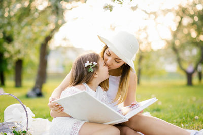 Mom and little daughter are looking at a family album with photos in the summer in the garden
