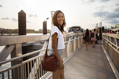 Portrait of smiling woman walking on pier against sky