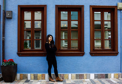 Full length portrait of woman standing against building