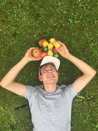 Young man lying with fruits on grassy field
