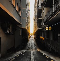 Empty road amidst buildings in city at sunset