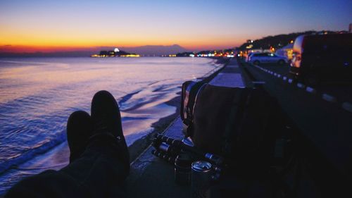 Low section of person on shore against sky during sunset