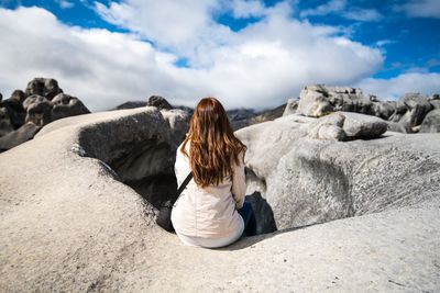 Rear view of woman sitting on rocks against sky