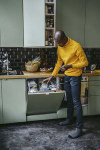 Full length of mid adult man doing dishes in kitchen at home