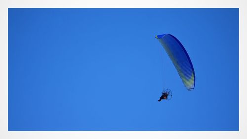 Low angle view of people paragliding against clear blue sky