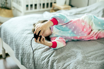 Girl playing video game while lying on bed at home