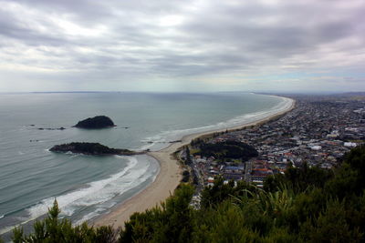 High angle view of sea by cityscape against cloudy sky