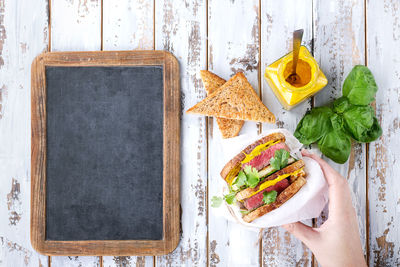 Cropped hand of woman holding sandwich over table