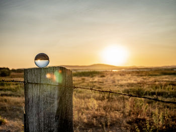 Wooden post on field against sky during sunset