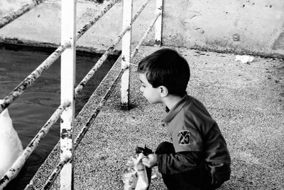 Boy holding packet crouching on promenade while looking through railing