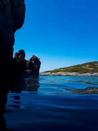 Rock formation in sea against clear blue sky