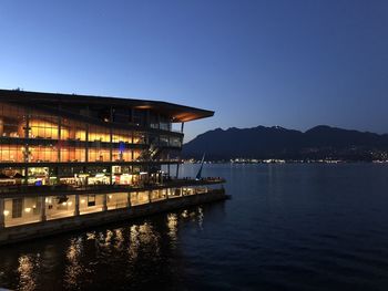 Illuminated building by sea against clear sky at night